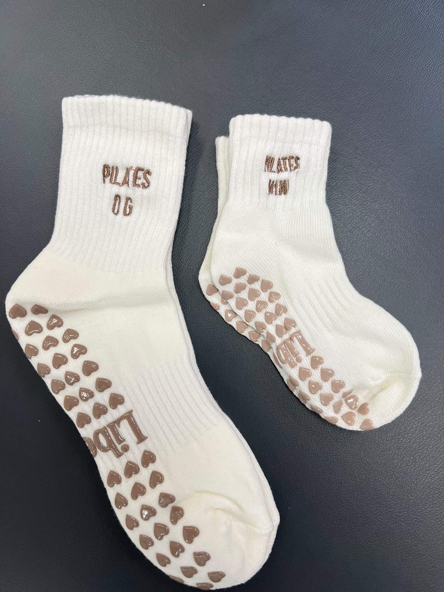 Matching cream grip socks — adult pair embroidered Pilates OG and child pair embroidered Pilates Mini, with heart-shaped grip soles